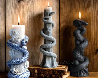 May include: Three decorative candles with a snake design. The candles are white, grey, and black. The white candle has a floral design. The candles are on a wooden surface.