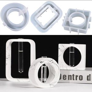 May include: Three white concrete vase molds with a marble pattern. The molds are in the shape of a square, a circle, and a rectangle. Each mold has a circular opening for a test tube.