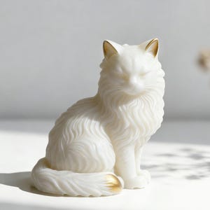 May include: A white cat figurine with gold accents on the ears and tail. The cat is sitting upright with its eyes closed, and its fur is detailed with wavy lines. The figurine is likely made of ceramic or a similar material.