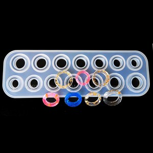 May include: A silicone mold with 15 ring-shaped cavities for making resin rings. The mold is white and has a rectangular shape. There are five resin rings in the image, each with a different color and design.