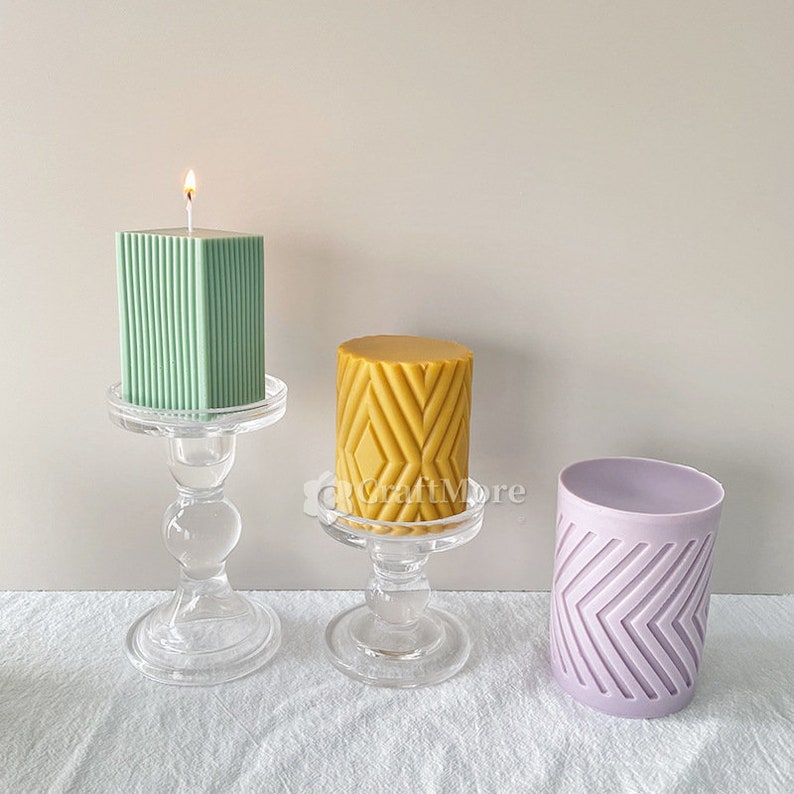 May include: Three candles on glass candle holders. The candles are different shapes and sizes. One candle is green and has vertical lines, one is yellow and has a diamond pattern, and one is purple and has a chevron pattern.