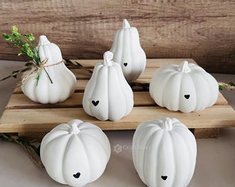 Peut inclure: Six citrouilles en céramique blanche avec des accents de cœur noirs. Les citrouilles sont disposées sur une surface en bois.