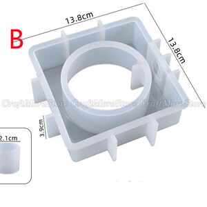 May include: White silicone mold for making candles. The mold is square with a round opening in the center. The mold measures 13.8 cm by 13.8 cm by 3.9 cm. A smaller silicone mold for making candles is also shown, measuring 1.9 cm in diameter and 2.1 cm in height.