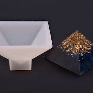 May include: A white silicone mold shaped like a pyramid, with a finished resin pyramid in the background. The resin pyramid is blue with gold flecks.