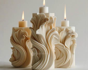 May include: Three ivory-colored, sculpted candle holders with lit candles. The candle holders have a square base and are adorned with a flowing, leaf-like design. The candles are white and have a soft, warm glow. The background is a plain, light color.