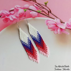 May include: A pair of long, beaded earrings with a red, white, and blue color scheme. The earrings are made of small, seed beads and have a fringe-like design.