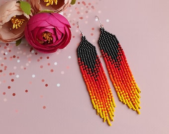 May include: A pair of long, beaded earrings with a black, orange, and yellow color gradient. The earrings are made with small, seed beads and have a fringe-like design.