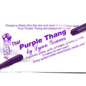 May include: A purple plastic tool with a slot, labeled "That Purple Thang by Lynn Graves." The tool is designed for pushing, poking, and pulling, and is accompanied by a card with instructions. The text says "Every quilter/crafter/seamstress needs one!"