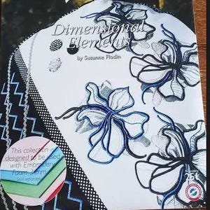 May include: A Husqvarna Viking Dimensional Elements embroidery design card by Susanne Flodin. The packaging features white fabric with black and blue embroidered floral motifs, zigzag patterns, and a circular inset showing colored foam sheets.