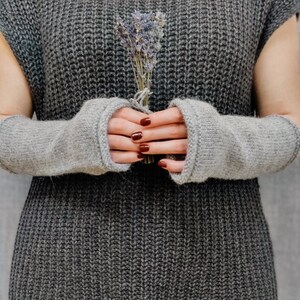 Può includere: Una persona indossa un maglione di lana grigio con scaldamani in lana grigi. La persona tiene un mazzo di lavanda secca.