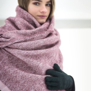 May include: A woman wearing a pink and white knitted scarf with a dark green knitted glove on one hand.