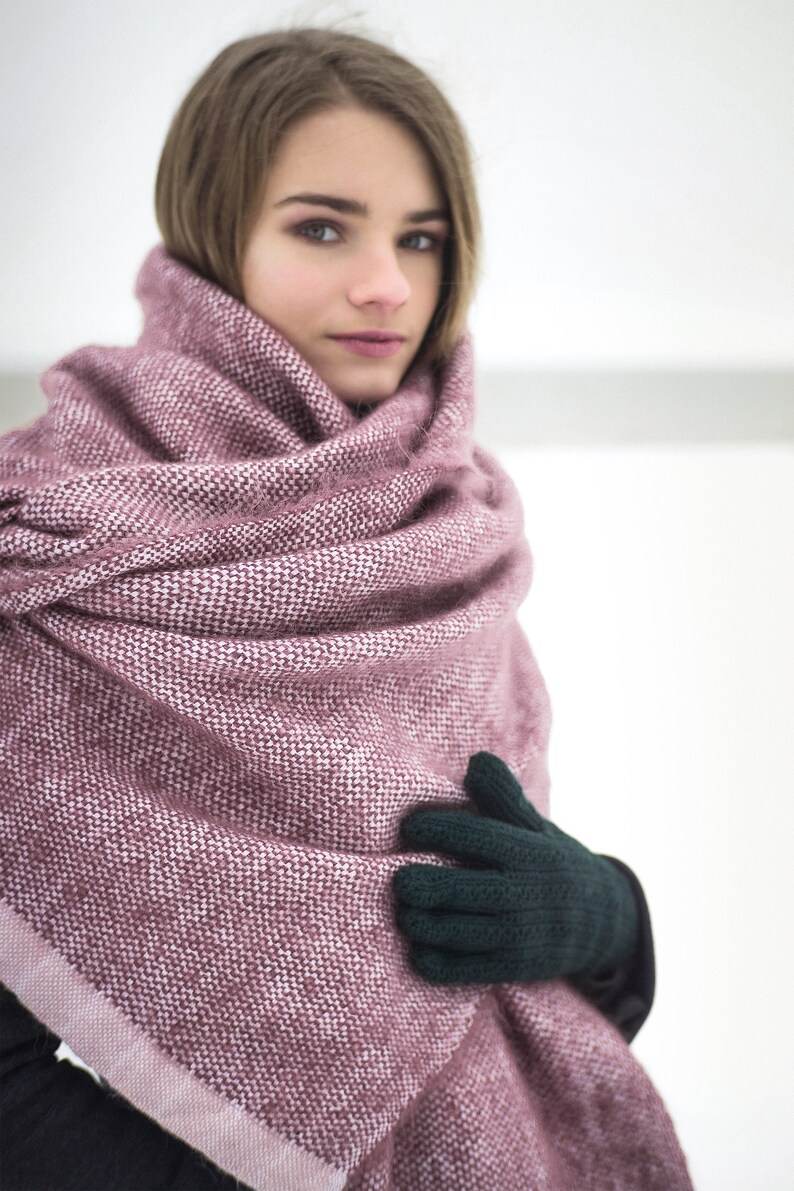 May include: A woman wearing a pink and white knitted scarf with a dark green knitted glove on one hand.