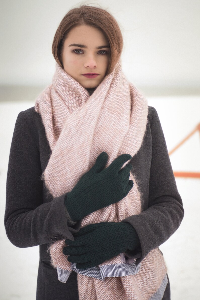 May include: A woman wearing a gray coat and a pink scarf with dark green gloves.