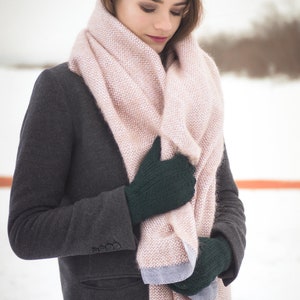 May include: A woman wearing a gray coat with a pink and white scarf wrapped around her neck. She is wearing dark green gloves and is holding the scarf in her hands.