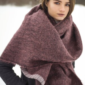 May include: A woman wearing a dark gray coat with a burgundy knitted scarf. The scarf has a white trim and is wrapped around her neck.