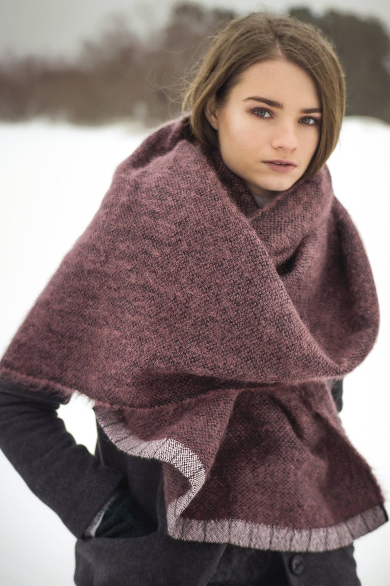 May include: A woman wearing a dark gray coat with a burgundy knitted scarf. The scarf has a white trim and is wrapped around her neck.