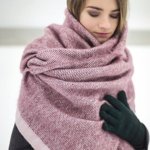 May include: A woman wearing a pink and white knitted scarf with a dark green knitted glove on her right hand.