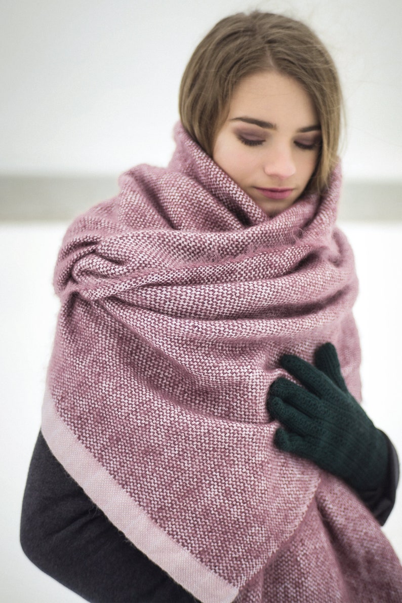 May include: A woman wearing a pink and white knitted scarf with a dark green knitted glove on her right hand.