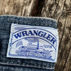 May include: A blue denim patch with white stitching and a white label that says "WRANGLER Born in USA" with a blue steamboat graphic.