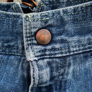 May include: Close-up of a blue denim fabric with a copper button. The button has a raised design with the word "Duncan" inscribed on it.