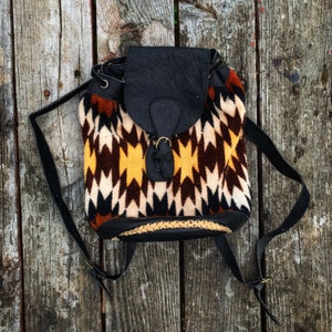 May include: A small black leather backpack with a geometric patterned fabric front. The fabric is brown, white, and yellow.