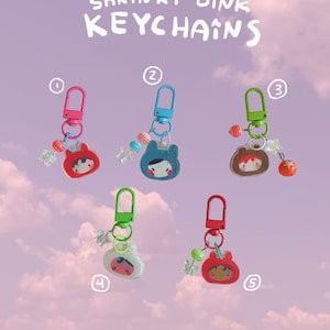 Puede incluir: Cinco llaveros hechos a mano Shrinky Dink numerados del uno al cinco. Cada uno cuenta con un cierre de plástico de colores, un dije de personaje y pequeñas cuentas decorativas con forma de estrella o esfera en tonos rosa, azul, verde y rojo.