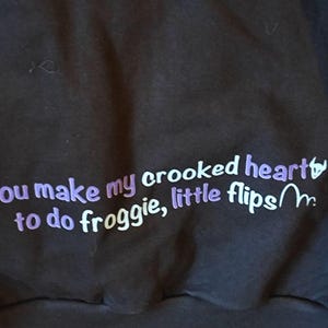 May include: A black sweatshirt with purple text that reads "You make my crooked heart to do froggy, little flips~m."