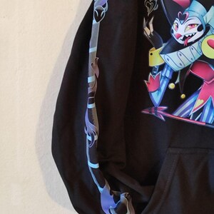 May include: Black hooded sweatshirt with a colorful cartoon character wearing a hat and a jester costume. The character has a long tongue and a mischievous expression. The sleeve has a blue and purple design.