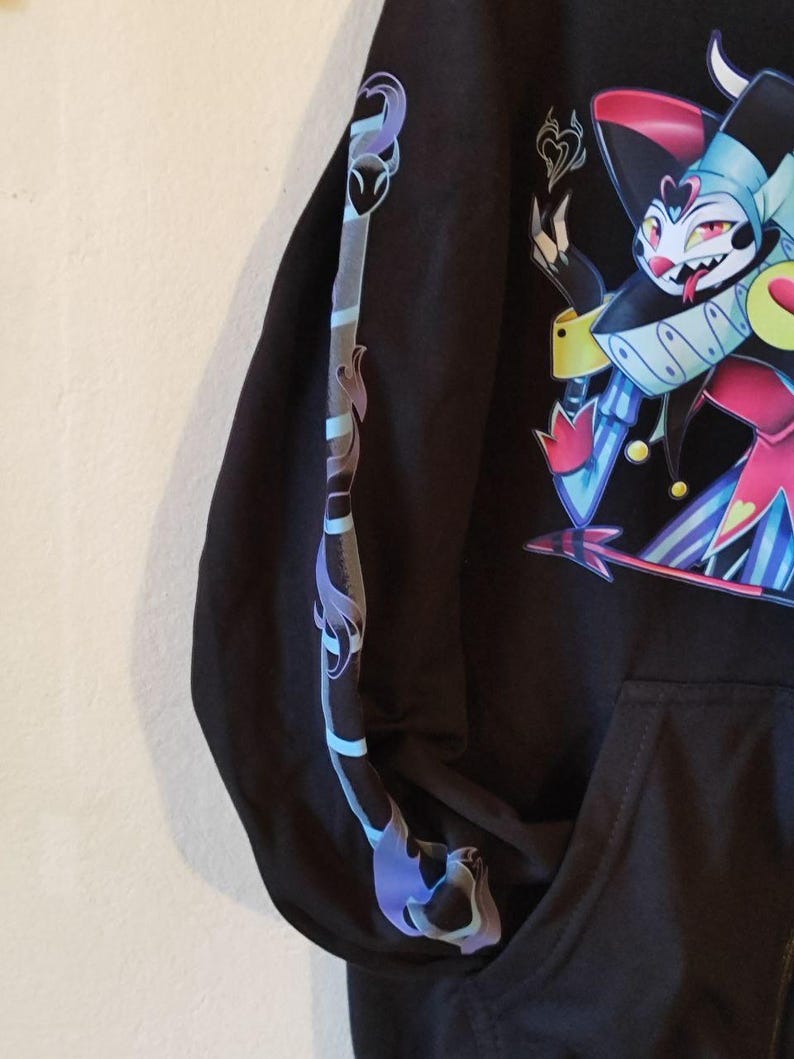 May include: Black hooded sweatshirt with a colorful cartoon character wearing a hat and a jester costume. The character has a long tongue and a mischievous expression. The sleeve has a blue and purple design.