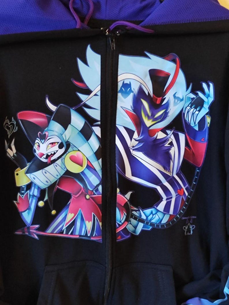 May include: Black zip-up hoodie with a colorful graphic print of two cartoon characters. The characters are a blue and red jester and a black and blue demon with a top hat. The hoodie has a purple hood.