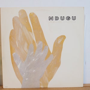 May include: A white record album cover with the title "NDUGU" in black text. The cover features a stylized image of two hands, one yellow and one gray, overlapping each other.