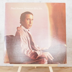 May include: A vinyl record album cover featuring a photo of Paul Simon. The album title is "Paul Simon - Greatest Hits, Etc."