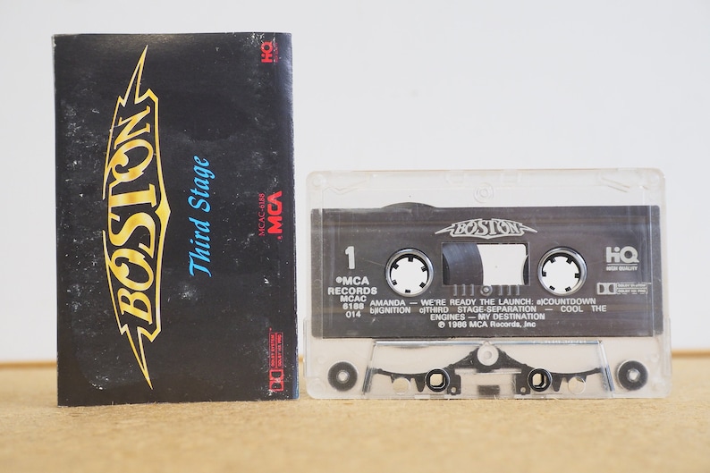 May include: A cassette tape with a black and white label that says "BOSTON" and "Third Stage". The cassette tape is in a clear plastic case. The label also includes the text "MCA Records", "MCAC", "Amanda", "We're Ready The Launch", "Countdown", "Third Stage Separation", "Engines - My Destination", "Cool The", and "1986 MCA Records, Inc."