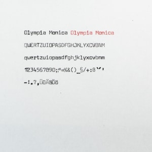 May include: A white sheet of paper featuring black typewriter text that reads Olympia Monica, followed by the QWERTZUIOPASDFGHJKLYXCVBNM alphabet in both uppercase and lowercase, numbers 1234567890, various punctuation marks, and the characters ÜÜÄÄÖÖ.