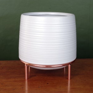 May include: White ceramic planter with a ribbed texture, sitting on a copper stand with three legs.