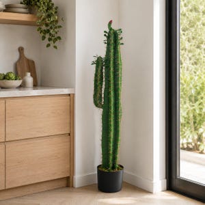 May include: A tall, green, columnar artificial cactus with a single side branch and a small red bud at the top. The cactus features vertical ridges with visible spines and is planted in a simple, cylindrical black pot standing on the floor.