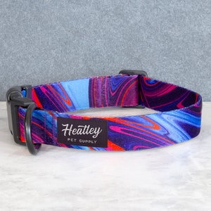 May include: A dog collar featuring a swirling abstract design in blue, purple, and orange. It has a black plastic buckle and a metal D-ring. The brand name "Heatley Pet Supply" is printed on a black label.
