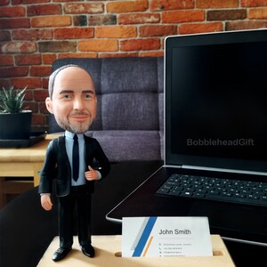 Business card holder on desk with male attorney figurine in business suite with business cards inside the base. Picture in office with laptop behind and beautiful brick wall.