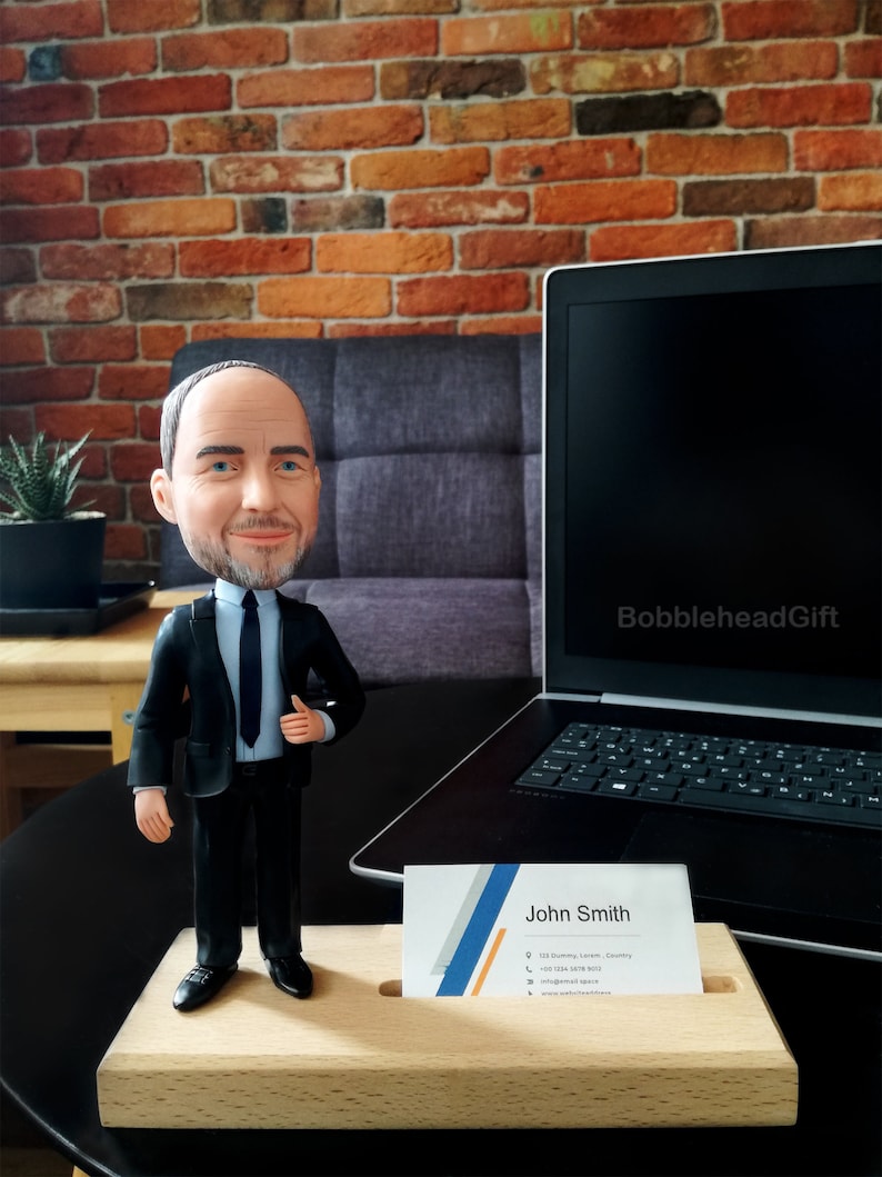 Business card holder on desk with male attorney figurine in business suite with business cards inside the base. Picture in office with laptop behind and beautiful brick wall.