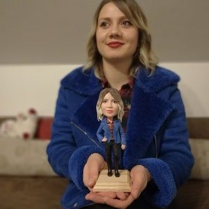 Woman in blue jacket holding her figurine in hands showing amazing similarity.