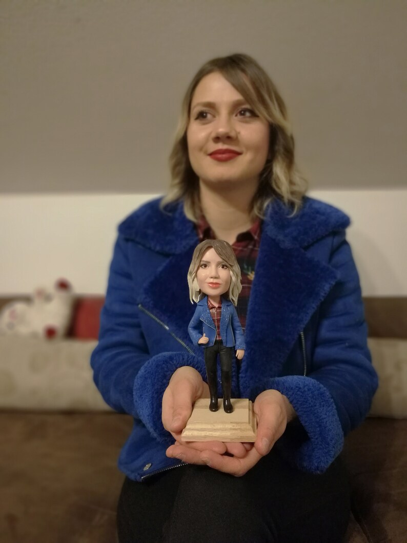 Woman in blue jacket holding her figurine in hands showing amazing similarity.