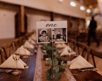 Puede incluir: Una tarjeta de número de mesa con la palabra "one" impresa en ella. La tarjeta está decorada con dos fotos en blanco y negro de niños. Las fotos están en un entorno rústico.