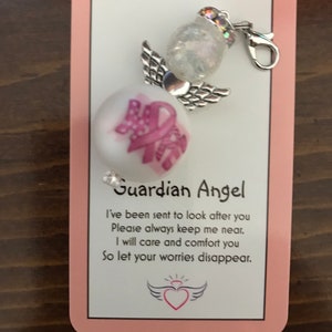May include: A white guardian angel charm with a pink ribbon and the text "Guardian Angel" on a pink card. The card reads "I've been sent to look after you. Please always keep me near. I will care and comfort you. So let your worries disappear."