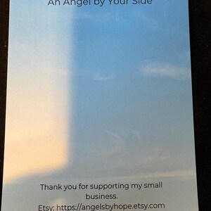 Puede incluir: Una tarjeta rectangular con un fondo tem&aacute;tico de cielo, con el texto "May There Always Be An Angel by Your Side." La parte inferior de la tarjeta dice "Thank you for supporting my small business." y la URL de la tienda Etsy.