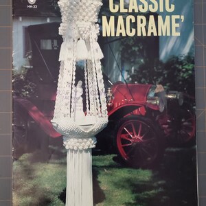 May include: A vintage book cover featuring a white macrame plant hanger with a bowl at the bottom. The book title is "Classic Macrame'" and the book number is "HH-33".