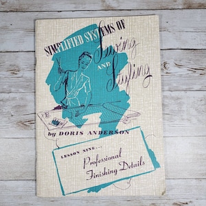May include: A vintage book titled "Simplified Systems of Sewing and Styling" by Doris Anderson. The cover features a woman sewing with a turquoise background and the text "Lesson Nine... Professional Finishing Details".