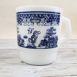 Op de afbeelding: Witte keramische mok met een blauw en wit wilgenmotief. Het motief toont een vogel, een boom en een huis.