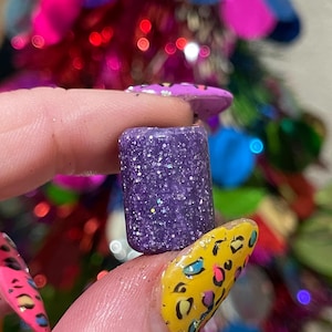 Könnte beinhalten: Ein kleines, violettes, glitzerndes, zylindrisches Objekt mit einer glatten Oberfläche.