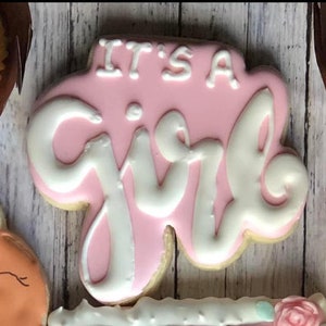 Puede incluir: Galletas rosa y blanca decoradas con las palabras "It's a Girl" en glaseado blanco.