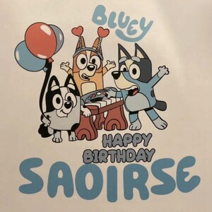 Könnte beinhalten: Ein Grafikdruck mit den Zeichentrickfiguren Bluey, Bingo und Muffin. Bingo spielt auf einem Keyboard und trägt ein Herz-Stirnband. Bluey steht rechts und Muffin links mit Luftballons. Der Text lautet Bluey Happy Birthday Saoirse.